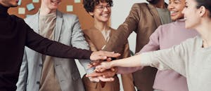 A group of happy, diverse colleagues celebrating teamwork and cooperation with a group high five indoors.