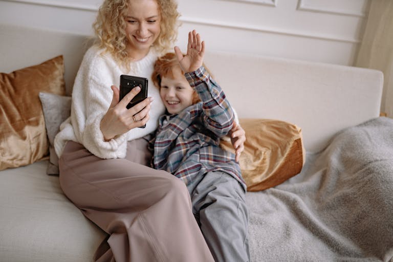 A mother and son smiling while sitting on a cozy sofa, sharing a happy moment indoors.