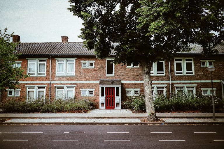 Classic brick apartment with red door and tree-lined street in Amsterdam suburb.