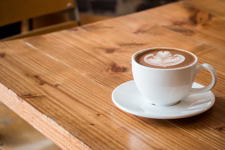 Close-up of a white cup of latte with artistic foam on a rustic wooden table.