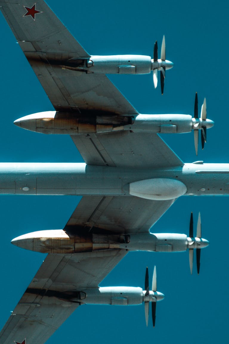 Low angle view of military aircraft with propellers against clear blue sky, emphasizing its sleek design.