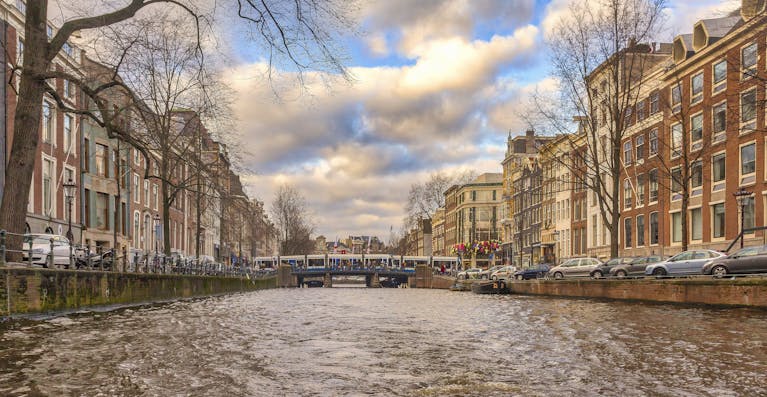 Picturesque view of Amsterdam canal lined with historic buildings and a bridge on a cloudy day.