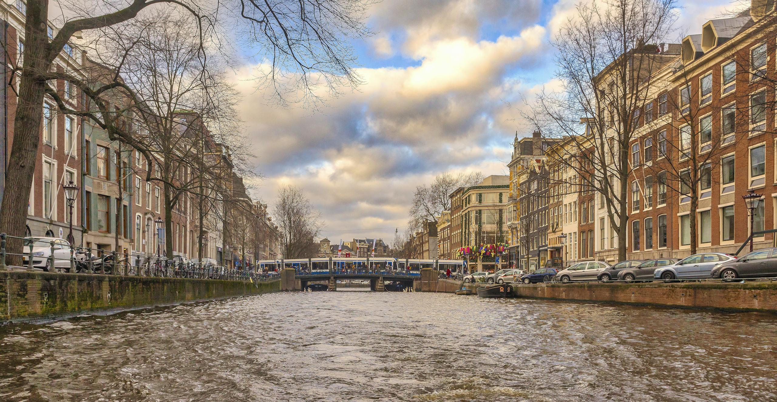 Picturesque view of Amsterdam canal lined with historic buildings and a bridge on a cloudy day.